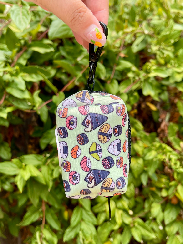 Poop bag holder dangling from hand, showing sushi print and clip