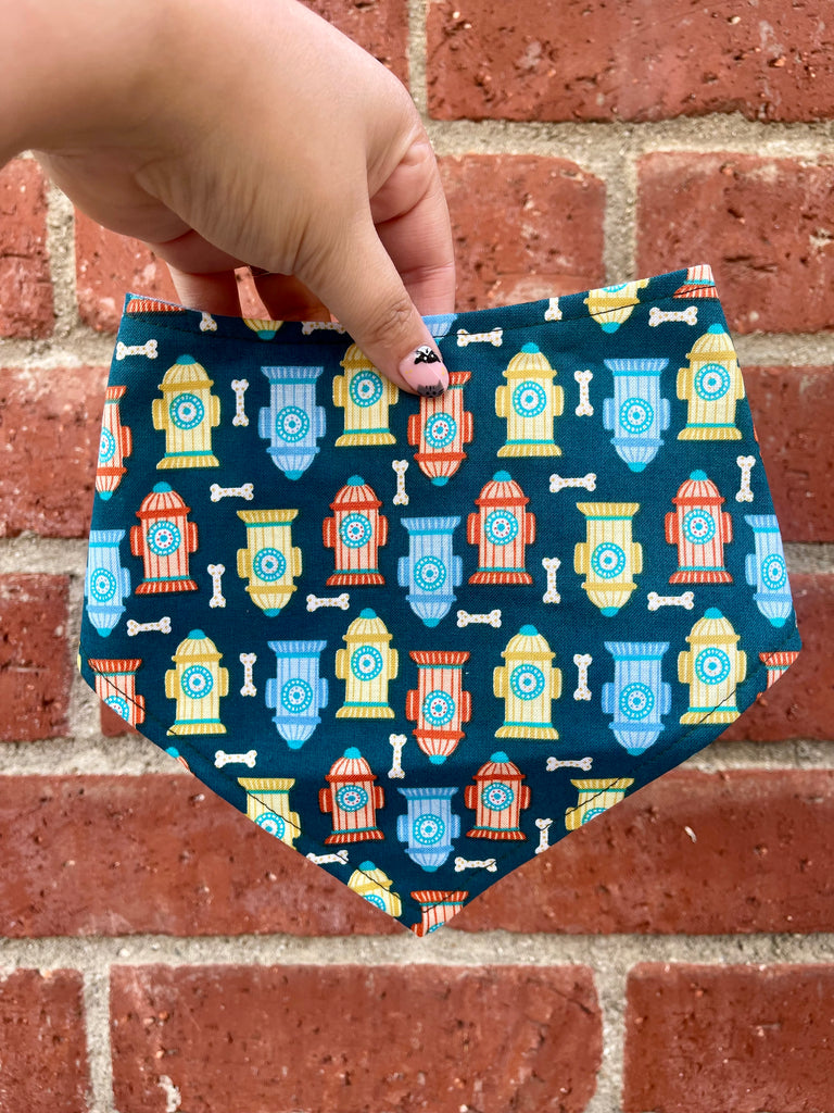 Hand holding “Sparky” dog bandana in front of red brick wall, showcasing colorful hydrant and bone pattern