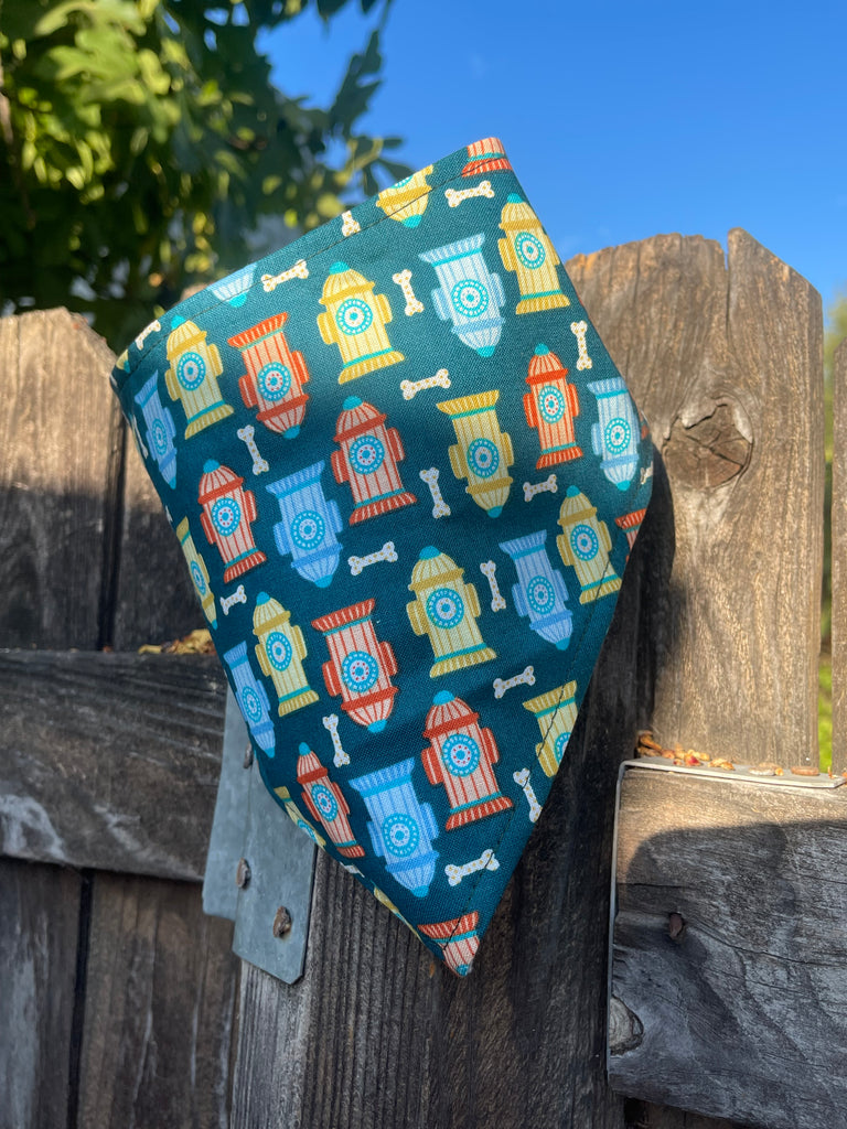 “Sparky” bandana draped on rustic wooden fence, vivid hydrant and bone pattern against blue sky backdrop
