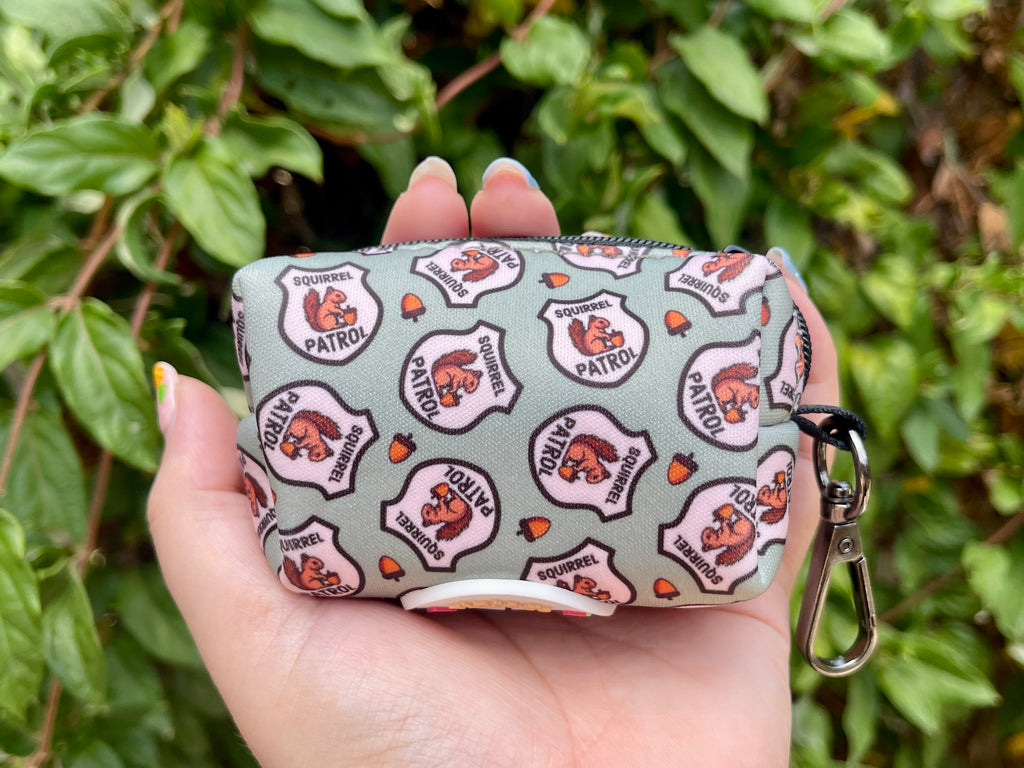 Hand holding squirrel poop bag holder against leafy greenery background
