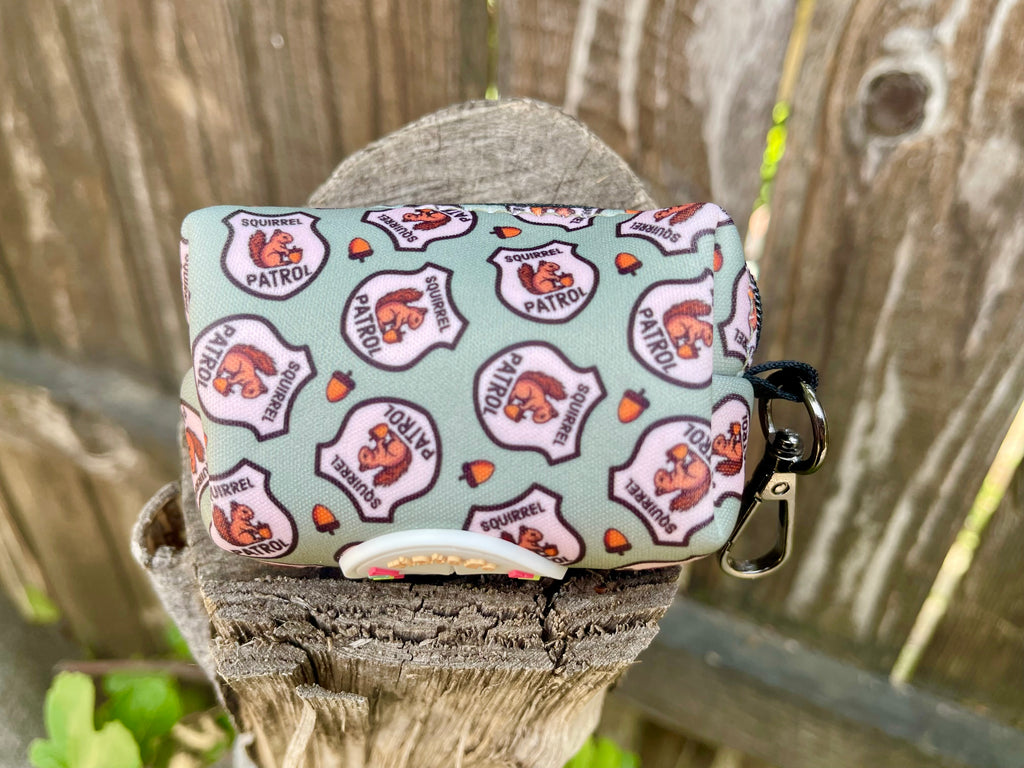 Squirrel Patrol poop bag holder resting on tree stump with acorn pattern visible