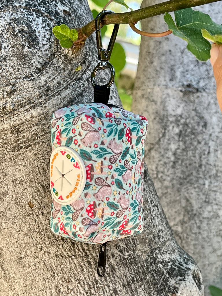 Stylish light green dog poop bag dispenser with adorable gray squirrel design, hanging conveniently for pet walkers.