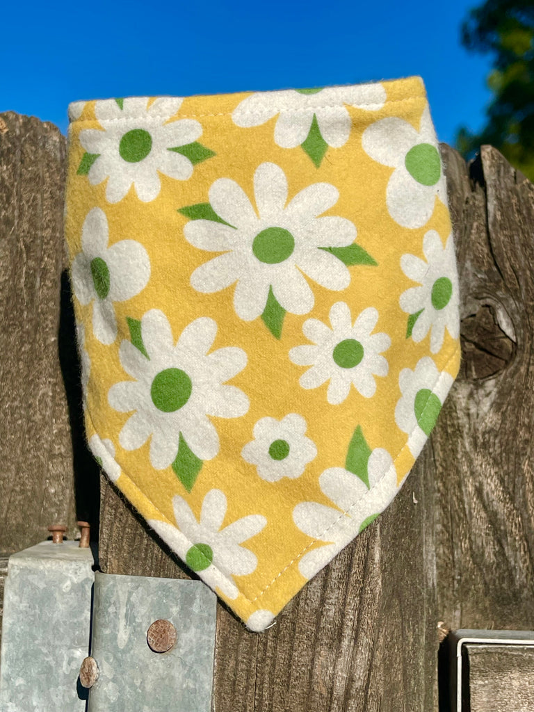 Snap-on dog bandana in a retro daisy print, laid flat on a wood fence. Stylish floral accessory for pets who love warm weather adventures.
