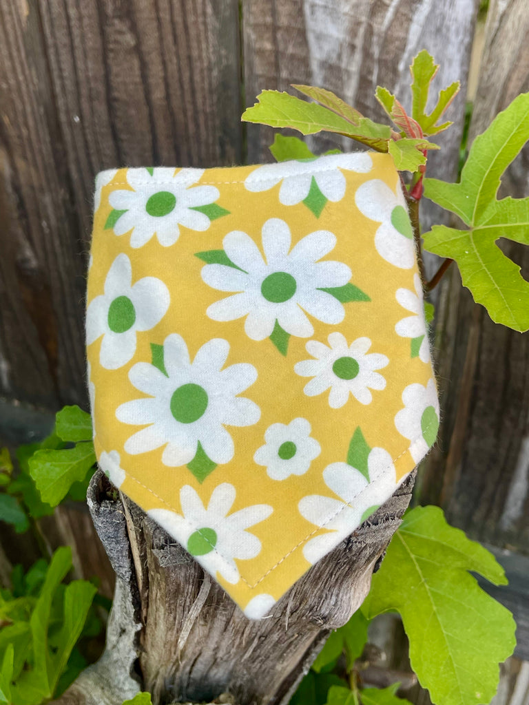 Snap-on dog bandana in a retro daisy print, laid flat on a wood fence. Stylish floral accessory for pets who love warm weather adventures.