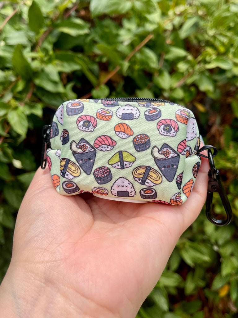 Hand holding sushi poop bag holder with green leafy background