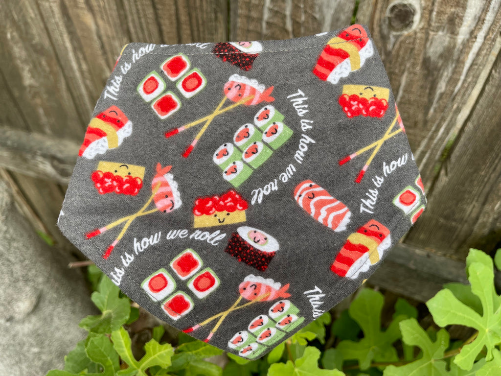 Snap-on dog bandana with “This is how we roll” sushi print, displayed on rustic wood