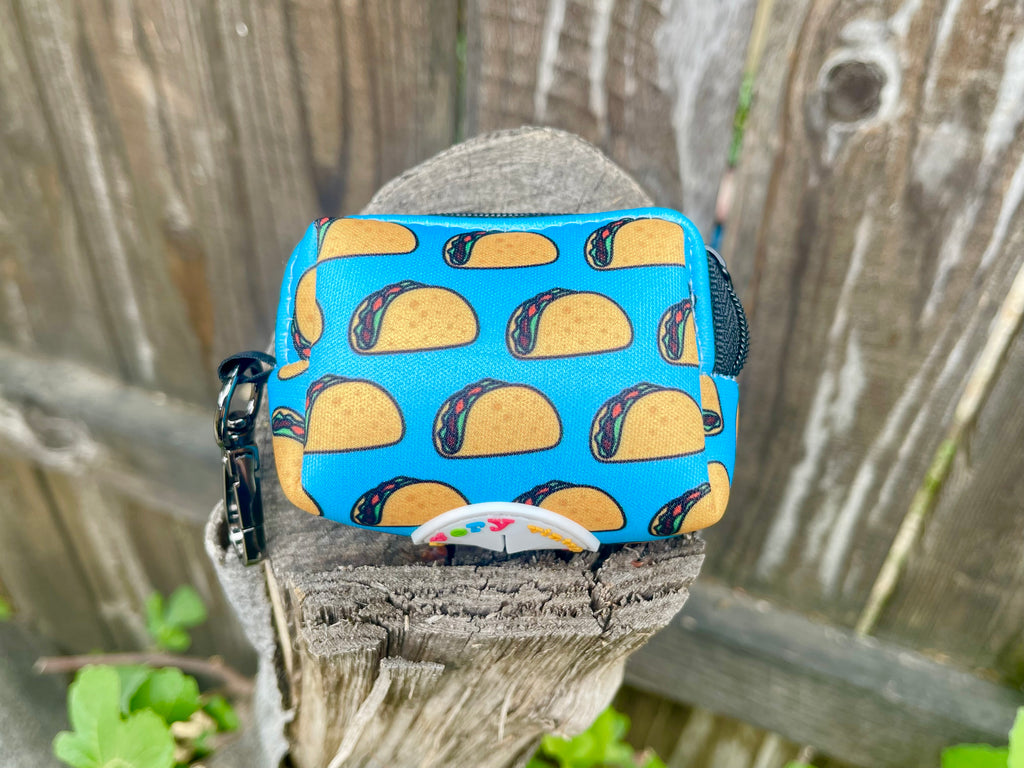 Taco poo bag holder sitting on a natural stump in front of greenery background