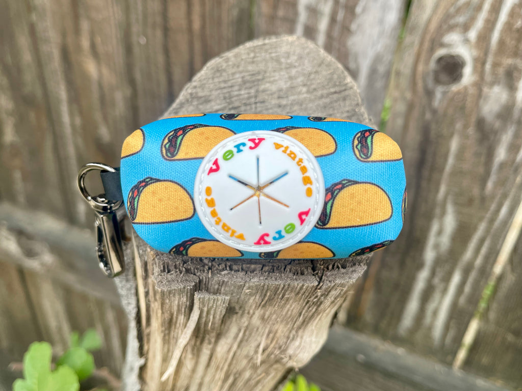 Bright blue with yellow taco Mexican food dog poop bag dispenser shown on a stump.