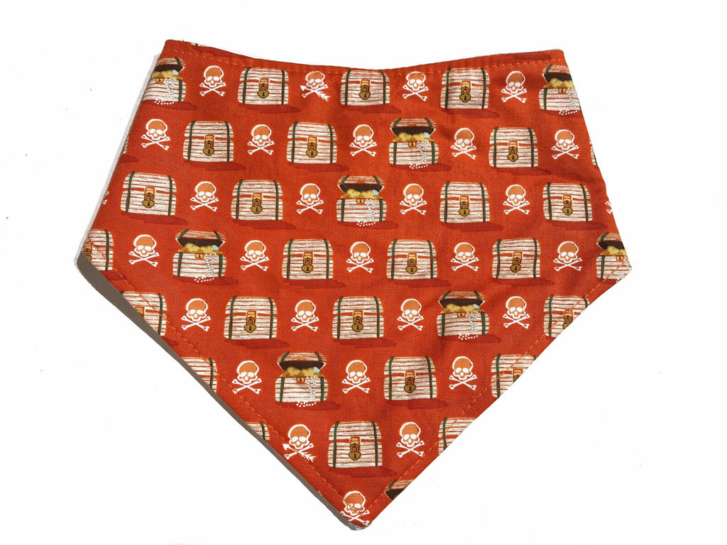 A pet bandana in a burnt orange cotton  with skulls and pirate treasure chests. Handmade in Los Angeles. Features 3 snaps on back of the bandana for a secure and adjustable fit.