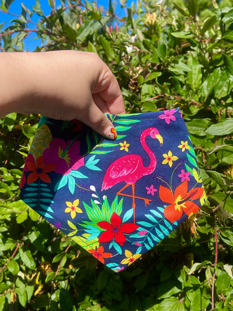 Colorful pet bandana with a pink flamingo and tropical flowers, held over a lush green background to highlight the vibrant summer design.