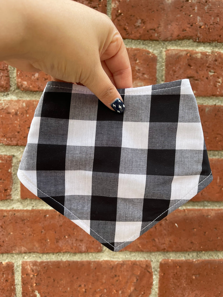 Black and white buffalo check dog bandana held in front of red brick wall