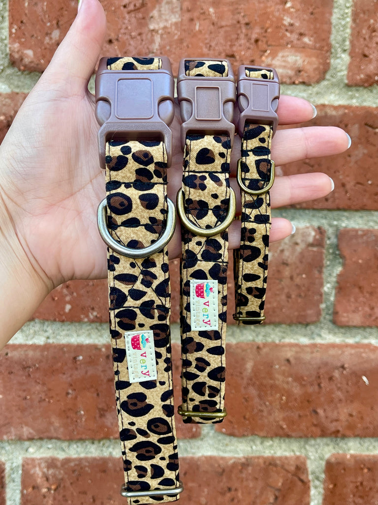 Leopard print dog collar with brown buckle and antique brass hardware, photographed against a rustic red brick wall. Handmade in Los Angeles.