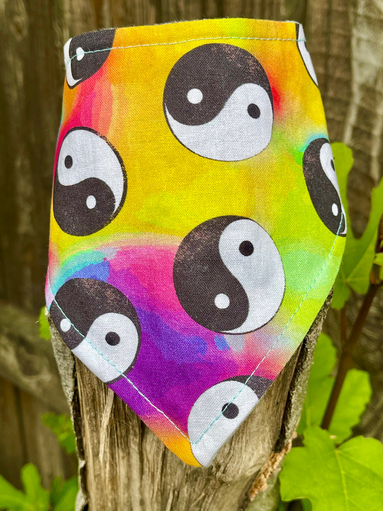 Bright tie-dye yin yang pet bandana displayed on a tree stump, highlighting vibrant colors and detailed fabric pattern.