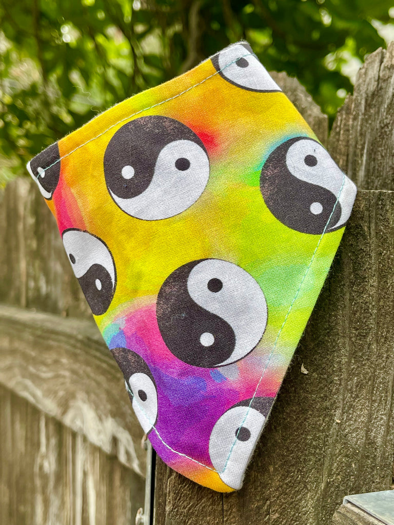 Eco-friendly pet bandana with black and white yin yang on vivid tie-dye background, styled on a rustic outdoor fence.