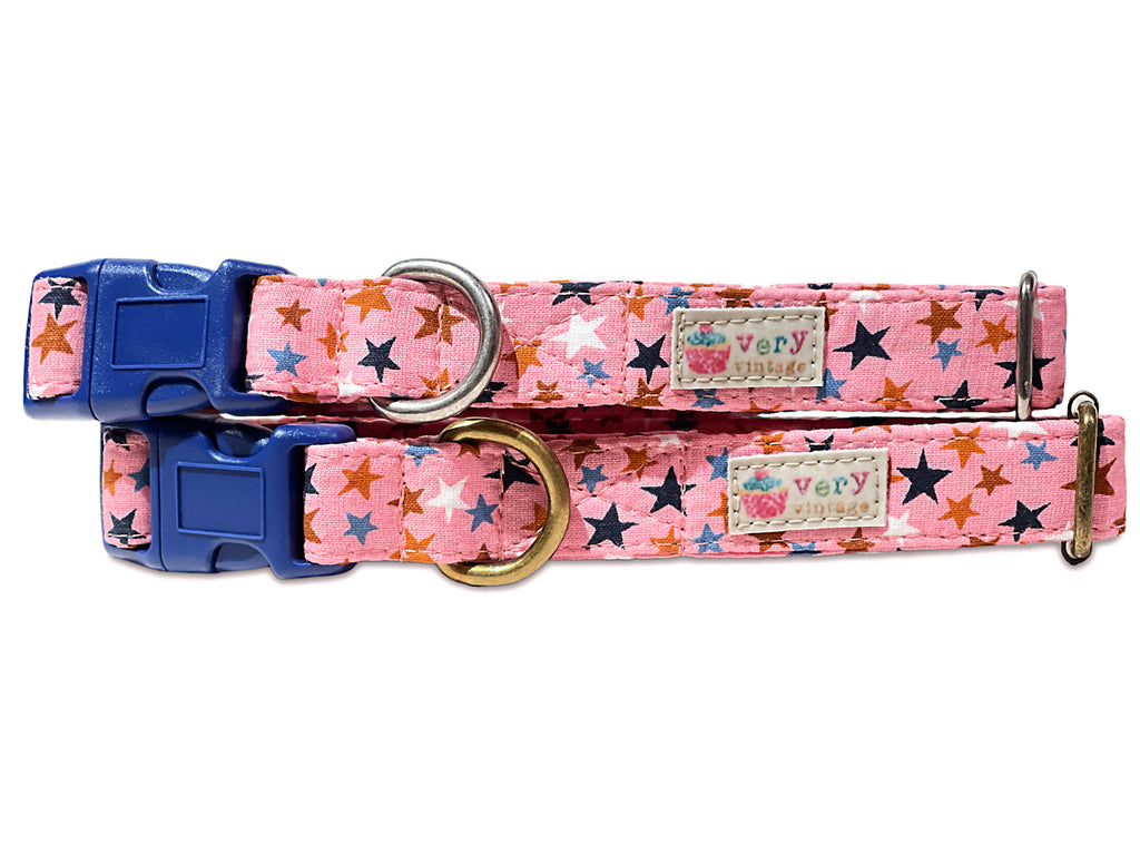 Close-up view of a handmade organic cotton dog collar featuring a playful pattern of colorful stars on a soft mauve pink background. Perfect for both dogs and cats, with options for custom sizes and antique brass or silver hardware.