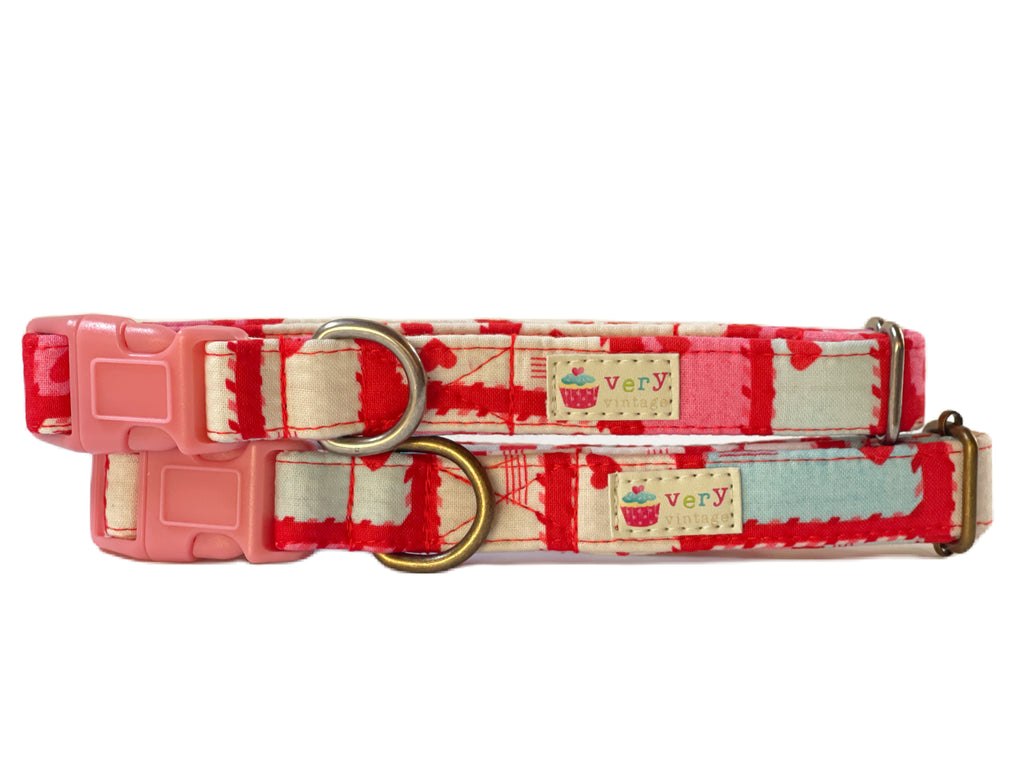 A close-up image of the "Love Letter" dog collar, showcasing its red background with colorful envelopes and hearts in pink, white, and blue. The collar is made from soft organic cotton with antique brass or silver hardware.