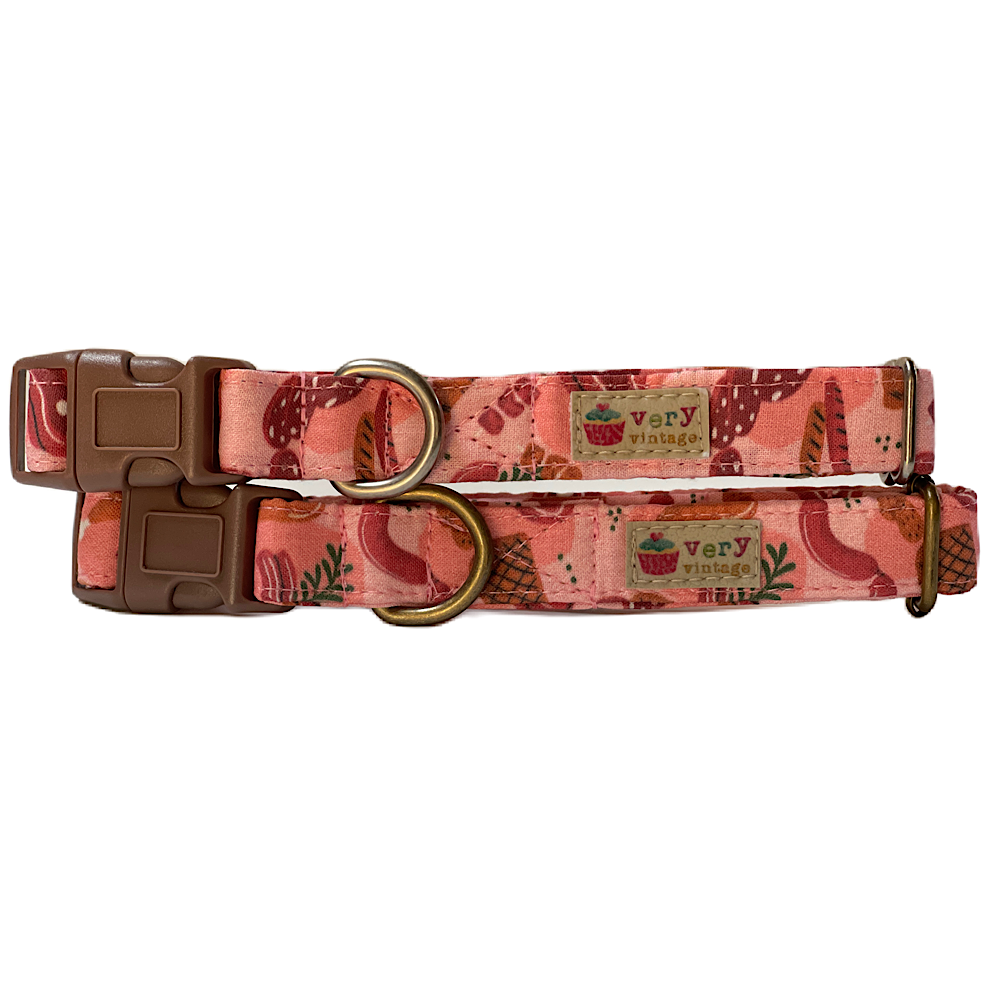 Handmade organic cotton dog collar featuring a light reddish-pink background adorned with a fun variety of different meats, including steaks, bacon, and sausages. Available in custom sizes for dogs and cats, with antique brass or silver hardware. 