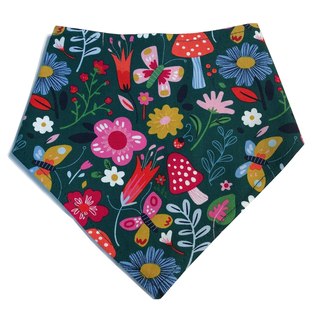 Handmade dog bandana with a dark green background featuring vibrant flowers, whimsical mushrooms, and butterflies, capturing an Alice in Wonderland-inspired design.